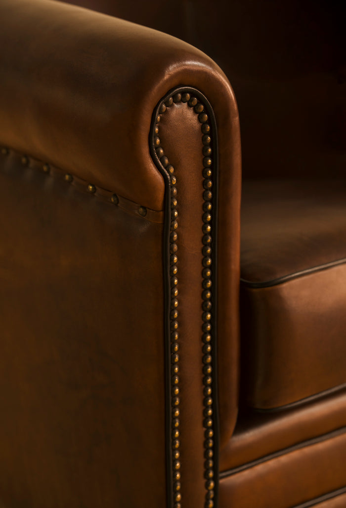 Close-up of a brown leather armchair with studded detailing.