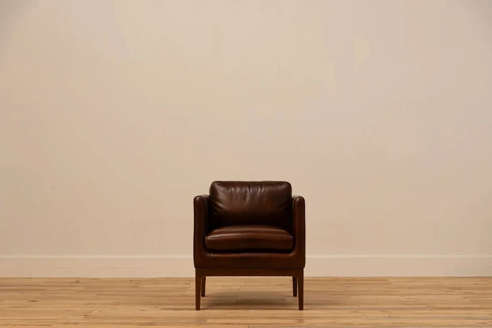 Shadow Claret  Full Grain Leather armchair with track arms and tapered wooden legs, set against a cream wall and light wood floor.