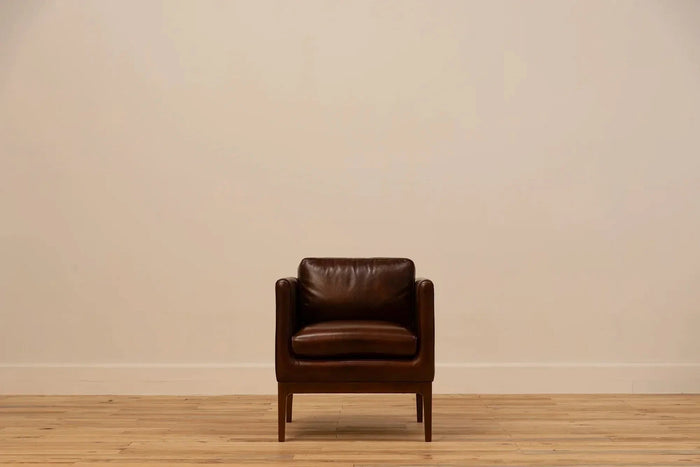Shadow Claret  Full Grain Leather armchair with track arms and tapered wooden legs, set against a cream wall and light wood floor.