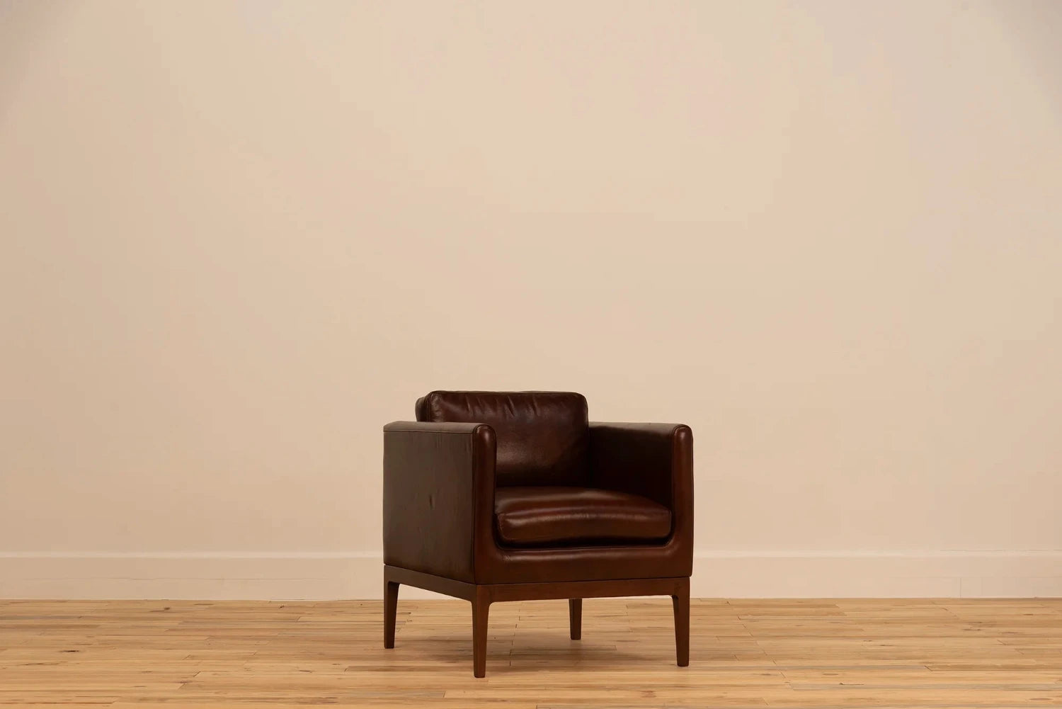 Shadow Claret  Full Grain Leather armchair with track arms and tapered wooden legs, set against a cream wall and light wood floor.