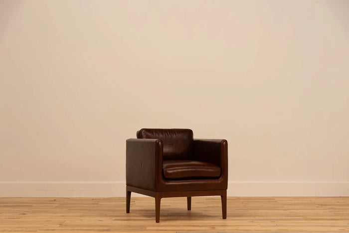 Shadow Claret  Full Grain Leather armchair with track arms and tapered wooden legs, set against a cream wall and light wood floor.