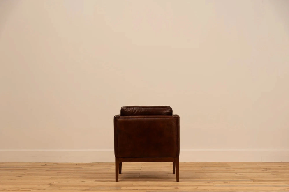 Shadow Claret Full Grain Leather armchair with track arms and tapered wooden legs, set against a cream wall and light wood floor.
