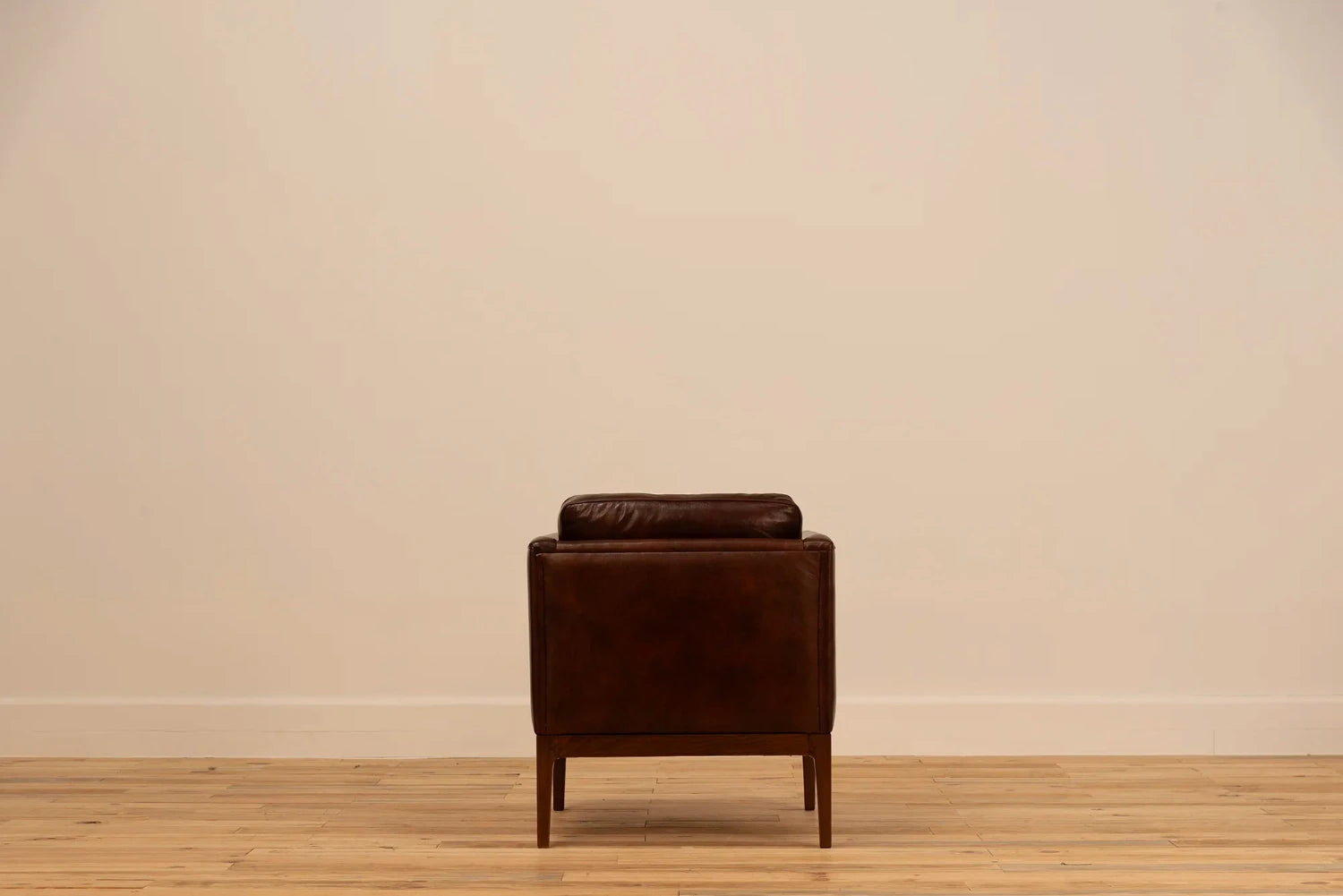 Shadow Claret Full Grain Leather armchair with track arms and tapered wooden legs, set against a cream wall and light wood floor.