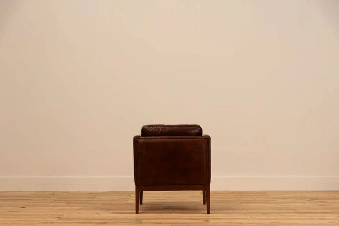 Shadow Claret Full Grain Leather armchair with track arms and tapered wooden legs, set against a cream wall and light wood floor.