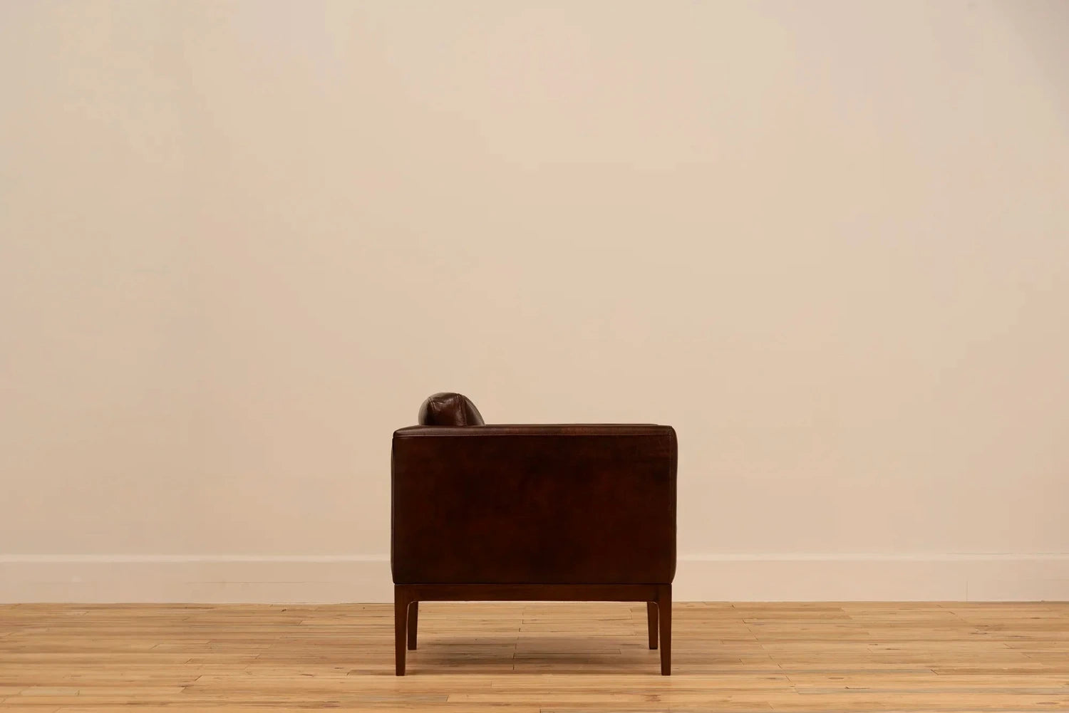 Shadow Claret Full Grain Leather armchair with track arms and tapered wooden legs, set against a cream wall and light wood floor.
