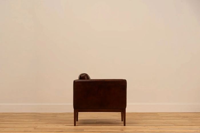 Shadow Claret Full Grain Leather armchair with track arms and tapered wooden legs, set against a cream wall and light wood floor.