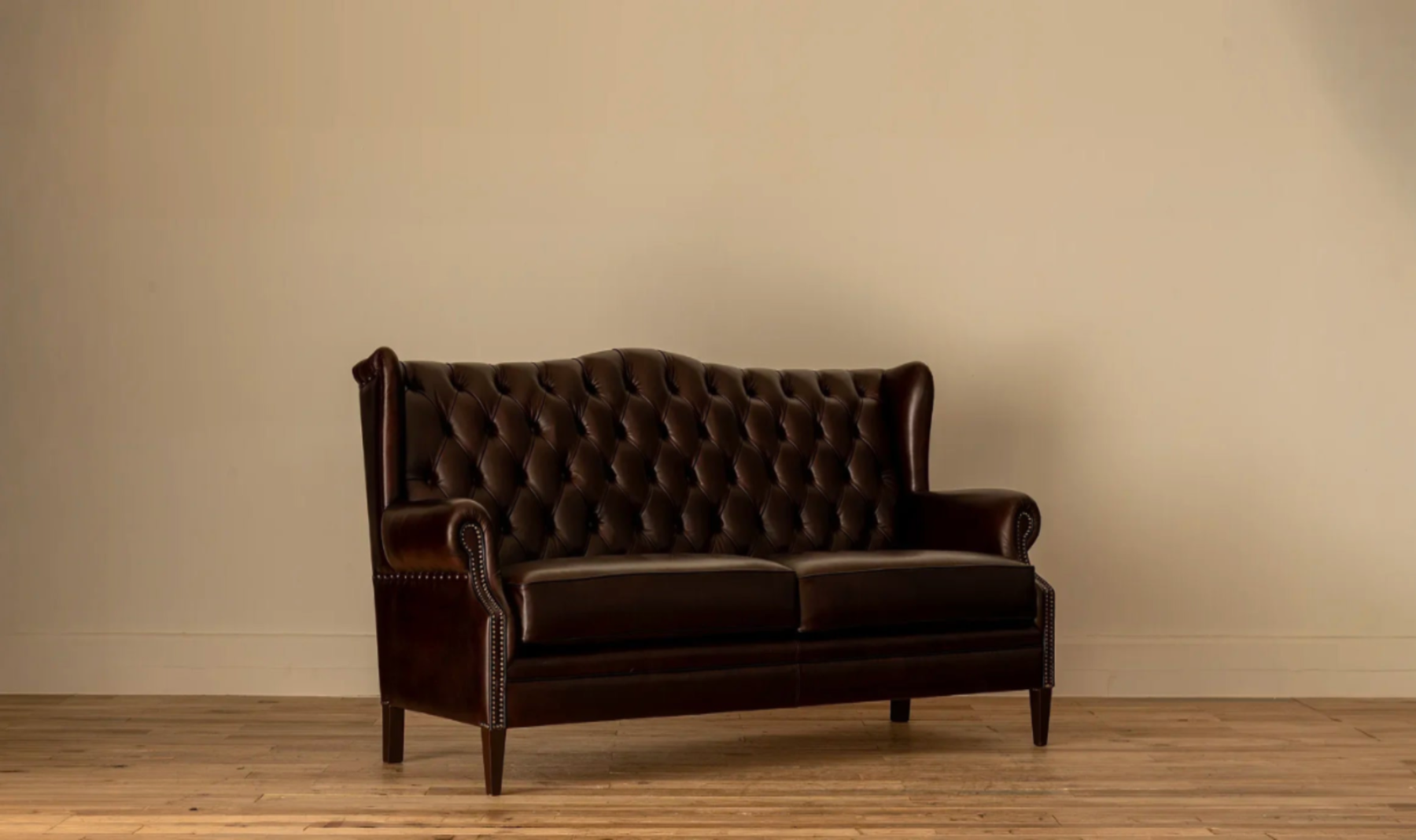 45-degree angle: Angled view of theJames Chesterfield 3-Seater Sofa in deep brown leather with diamond button tufting, rolled wingback arms, and nailhead trim, on tapered wood legs.