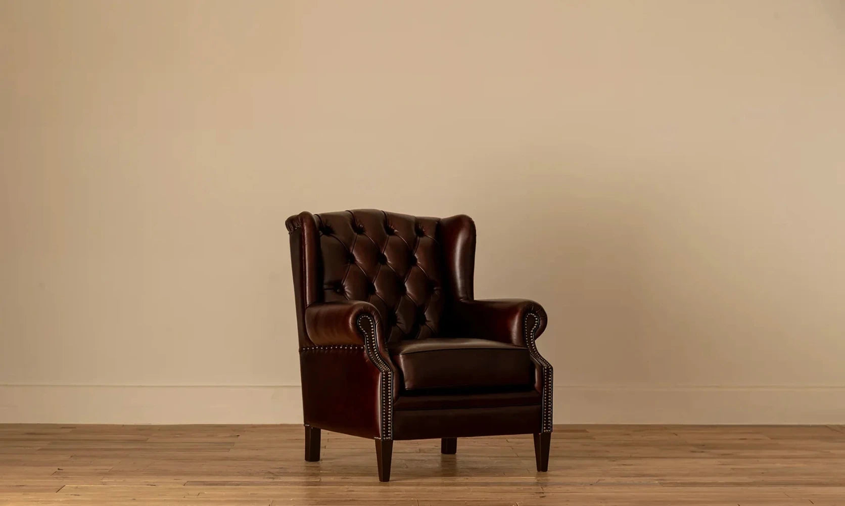 45-degree angle: "Angled view of the James Chesterfield wingback armchair showing its tufted backrest and rolled arms with nailhead detailing.