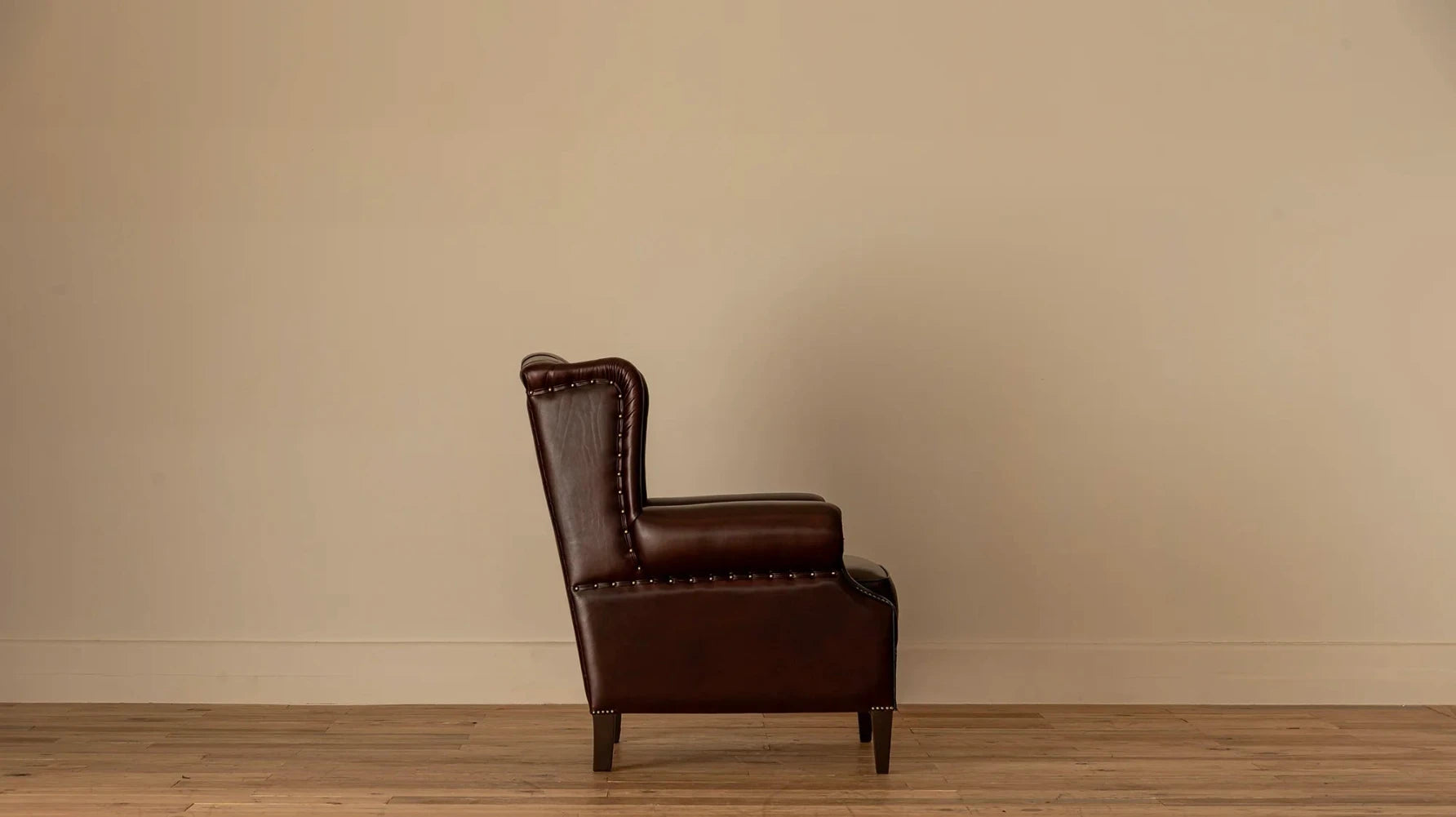 Side view: "Side profile of the James Chesterfield wingback armchair showing its high tufted back, rolled arm, and nailhead trim