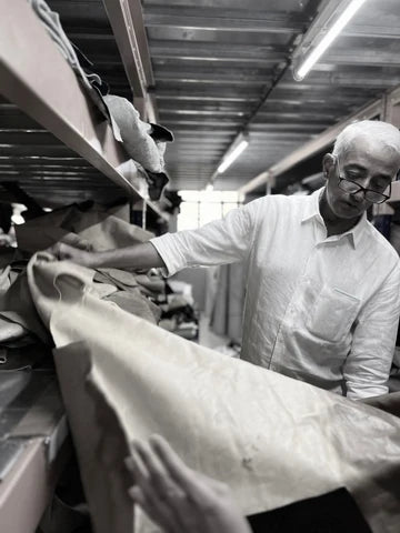 Chester’s founder examining a sheet of leather inside the workshop, surrounded by materials used to create the brand’s handcrafted furniture.