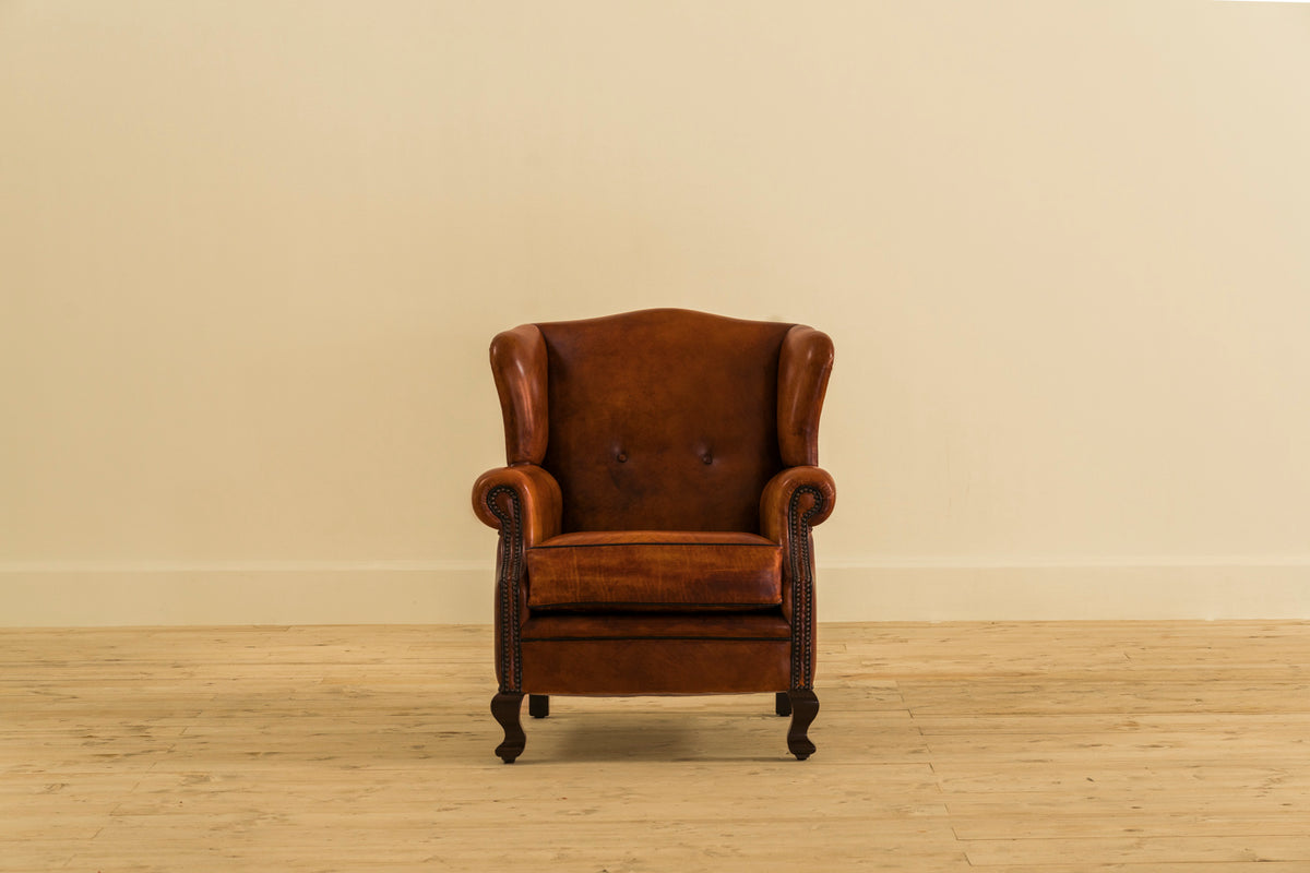 John Wood the Elder wingback armchair by Chester's India in aged Shadow Wet Bark leather, with a high back, protective wings and brass tack detailing.